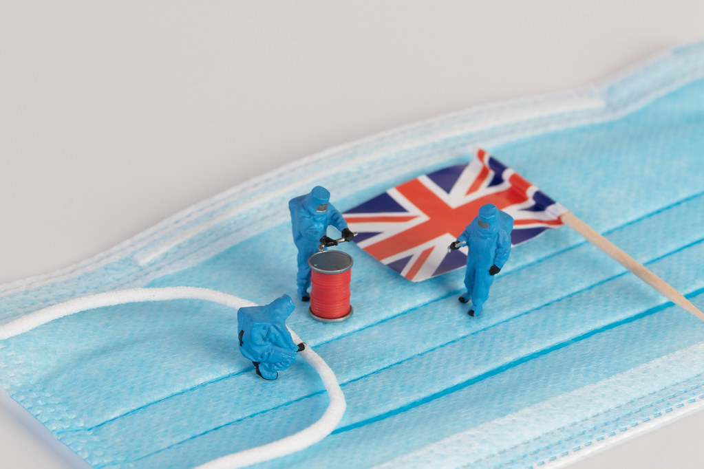 Miniature workers in protective clothes on a medical mask with flag of United Kingdom