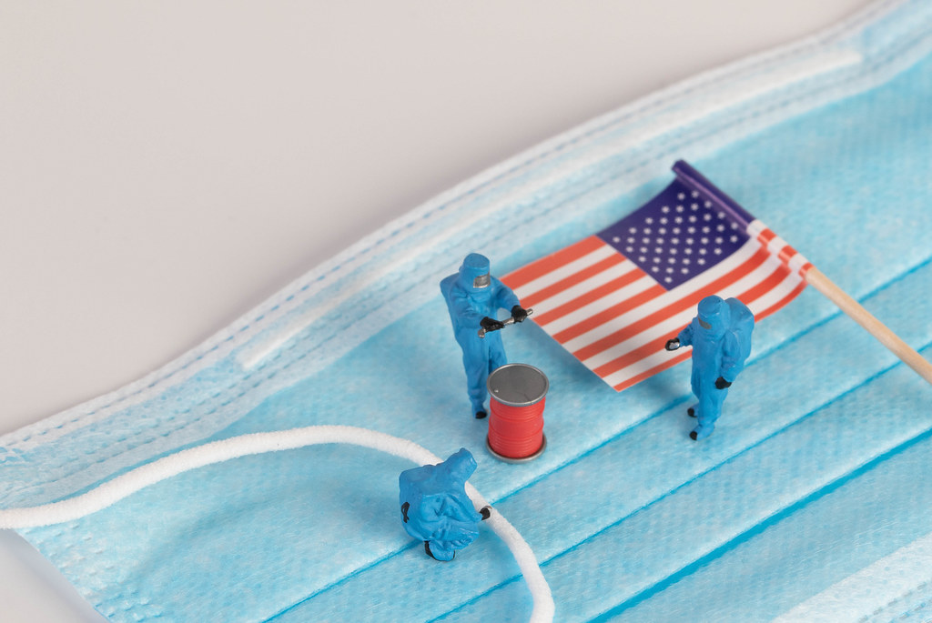 Miniature workers in protective clothes on a medical mask with flag of Unites States of America