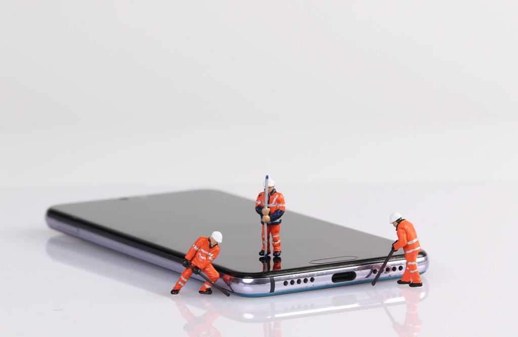 Miniature workers repairing smartphone on white table