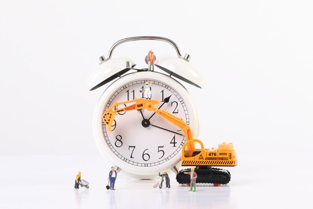 Miniature workers wtih excavator and alarm clock on white background
