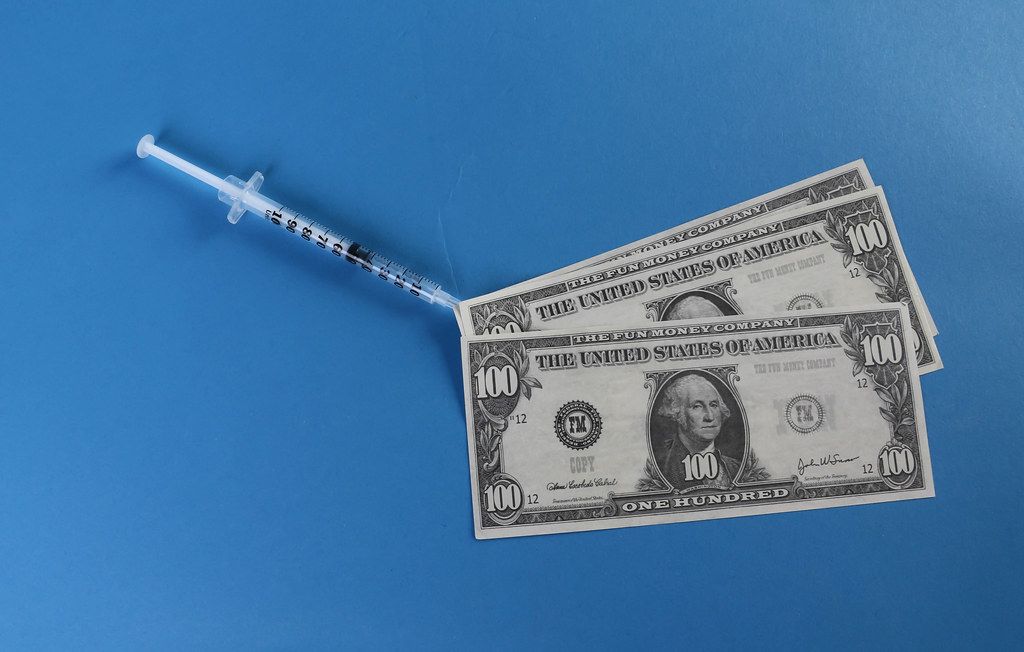 Money and syringe on blue background