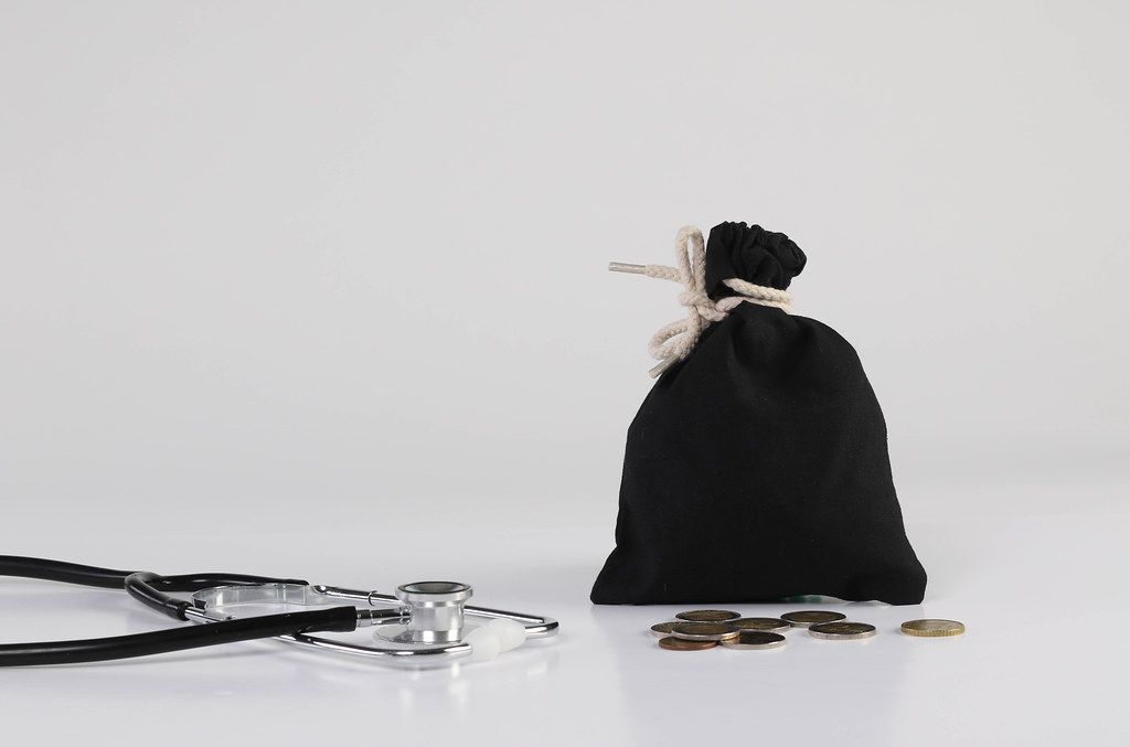 Money bag with coins and stethoscope on white background