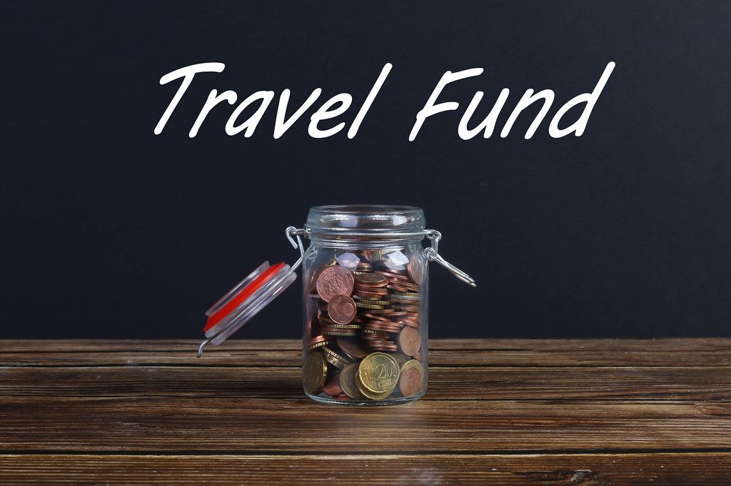 Money jar on wooden table with Travel Fund text