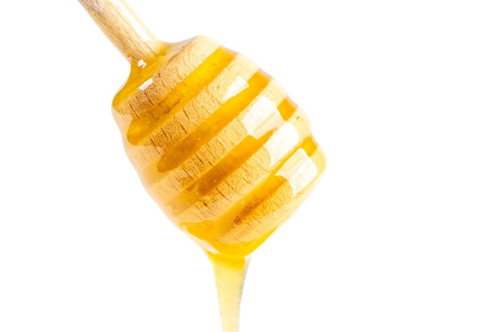 Natural bee honey flows down a wooden honey dipper