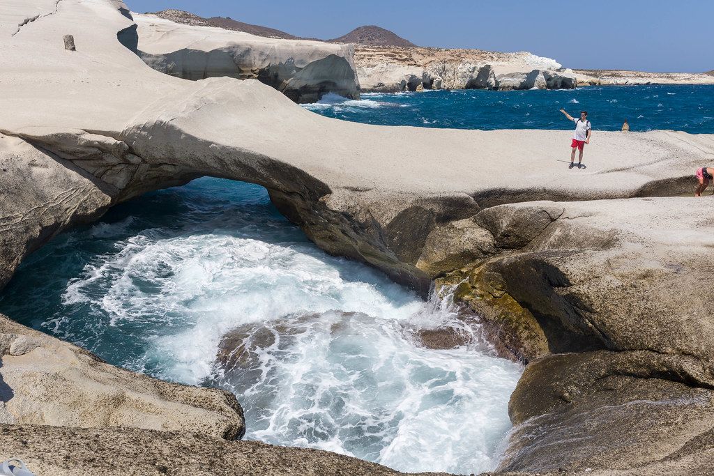 Naturbogen an der Nordküste Milos mit rauem Meer und Touristen. Urlaub auf Milos, Griechenland