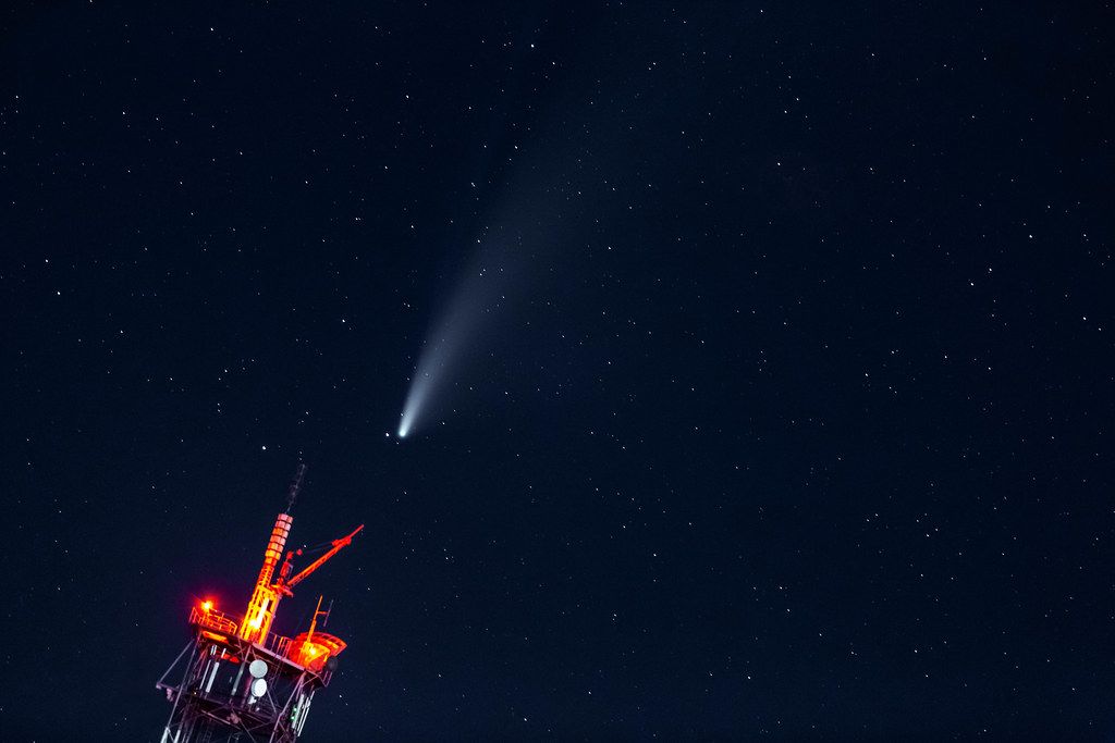 Neowise Comet approaching the earth over a TV tower in the dark night sky with stars