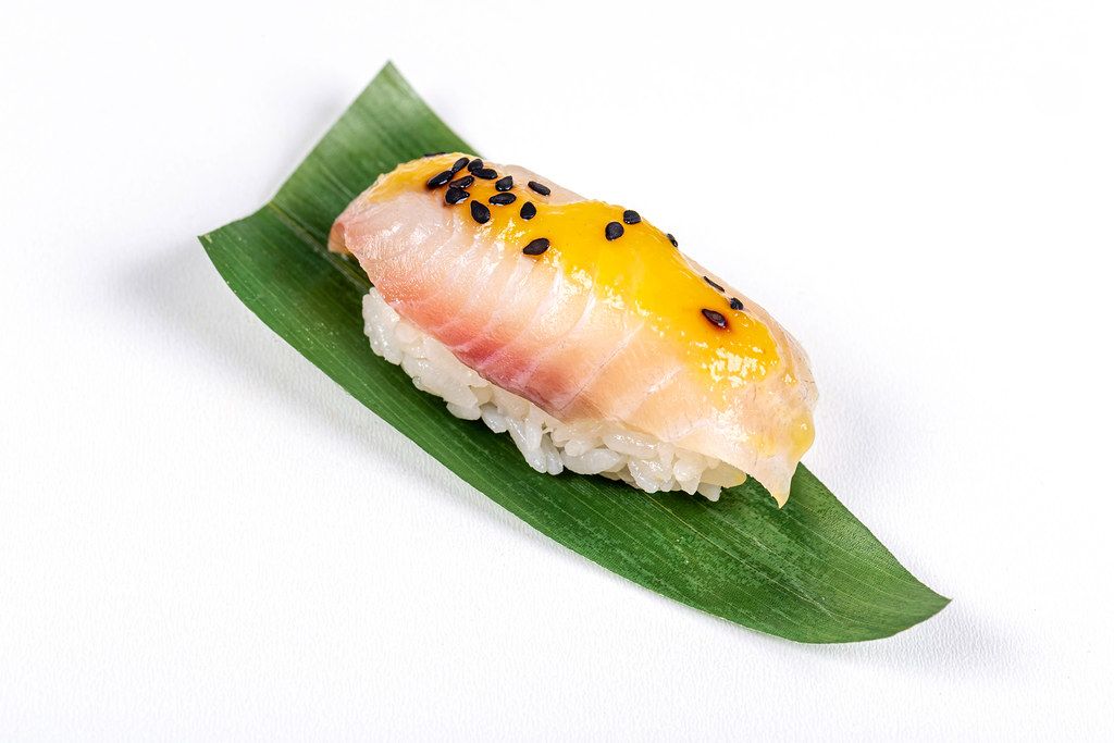 Nigiri with sea bass fillet and mango sauce on green leaf