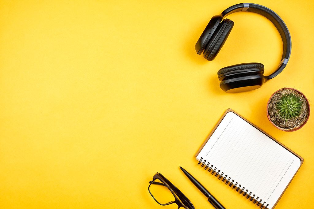 Notebook with wireless headphones on a yellow desk