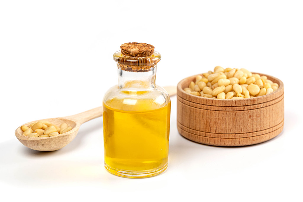Oil in a bottle with pine nuts in a wooden spoon and in a bowl on a white background