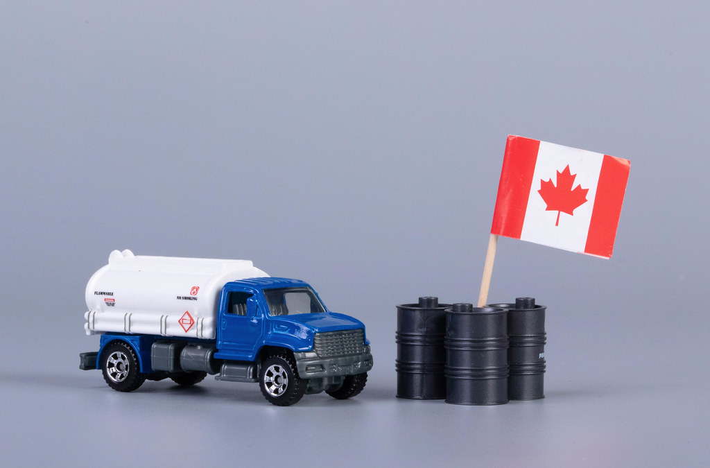 Oil truck and oil barrels with flag of Canada on grey background