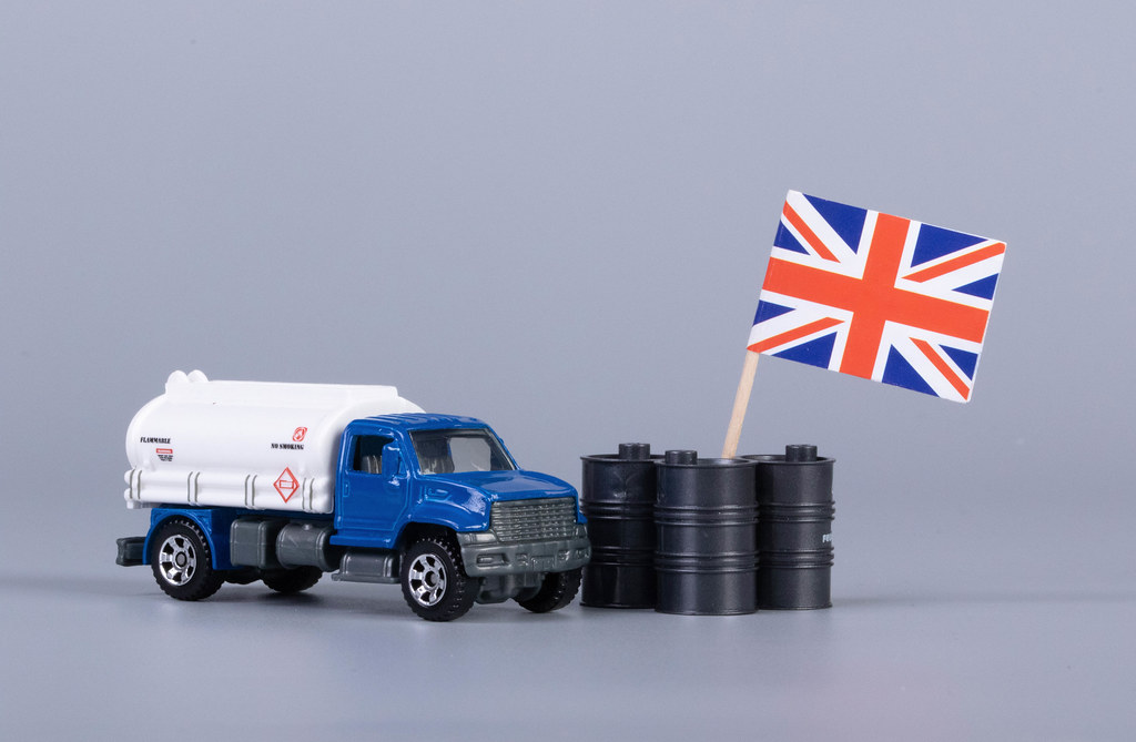 Oil truck and oil barrels with flag of United Kingdom on grey background