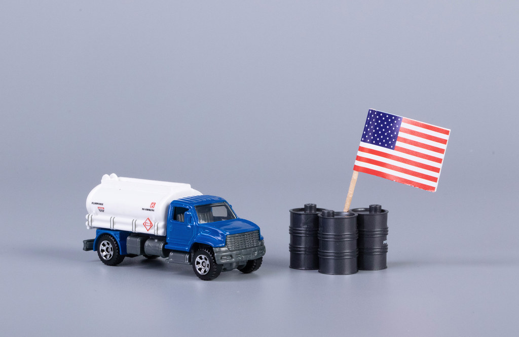 Oil truck and oil barrels with flag of United States of America on grey background
