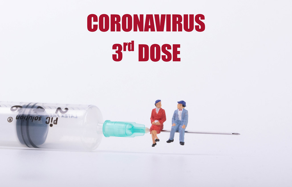 Older couple sitting on a syringe and Coronavirus 3rd dose text