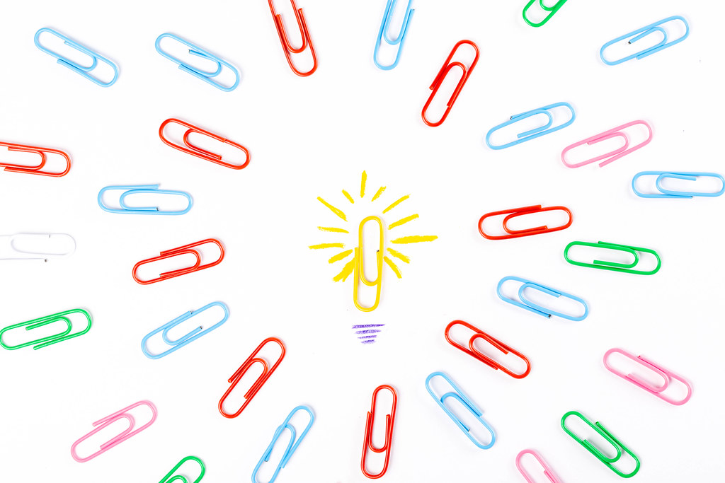 One light bulb made from paper clip surrounded by many multicolored paper clips, business concept