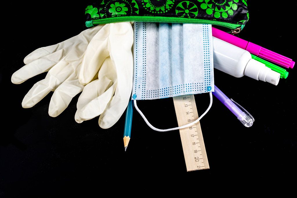 Open pencil case with school supplies, rubber gloves and mask on black background
