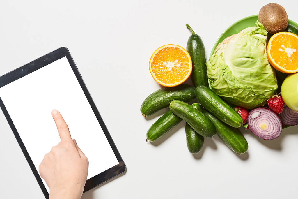 Organic vegetables, fruits and a person using tablet with a blank screen