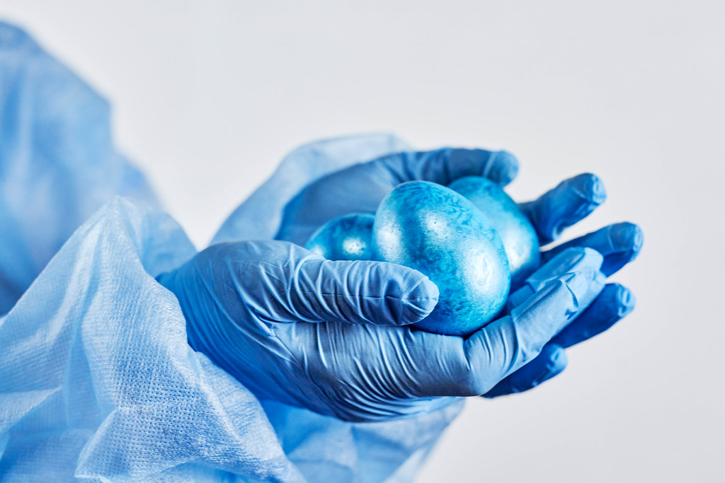 Ostern in Corona-Zeiten: blaue Ostereier in den Händen mit Einmalhandschuhen und Schutzkleidung