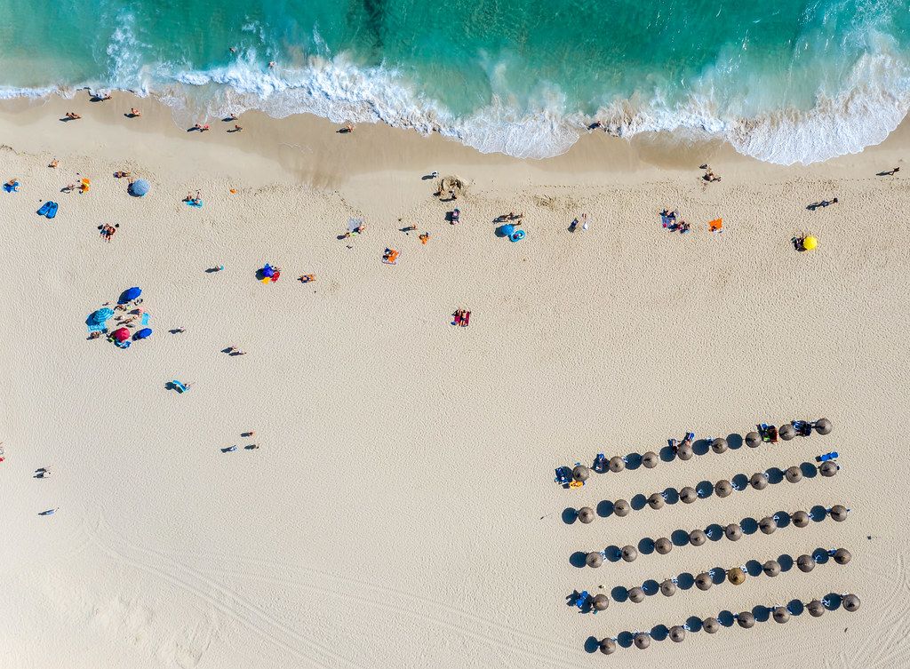 Overhead drone photo of Mallorca beach Cala Mesquida with umbrellas, waves, sand and tourists