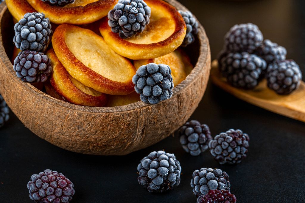 Pancakes in a wooden bowl with blackberries, close-up