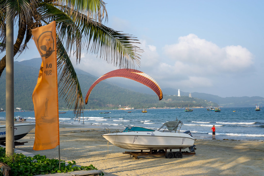 Paraglider landing next to a Speedboat on My Khe Beach with Linh Ung Pagoda on Son Tra Island in the Background in Da Nang, Vietnam