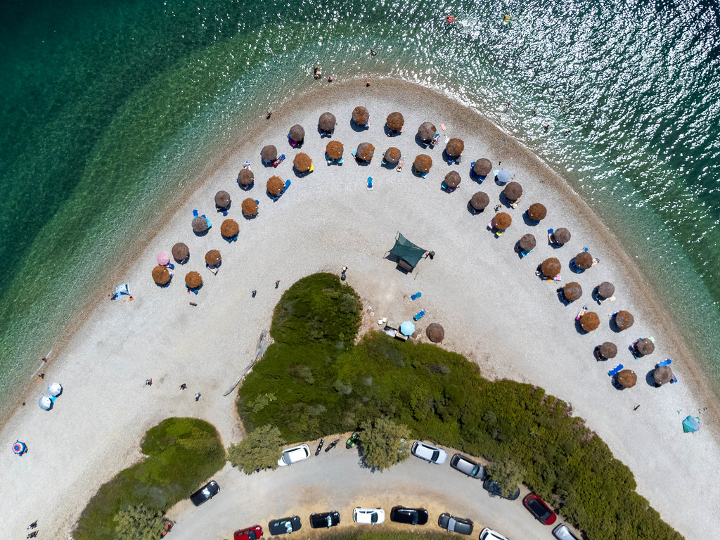 Parking spaces and straw parasols on the pebble beach of Agios Dimitrios with turquoise waters. Top view