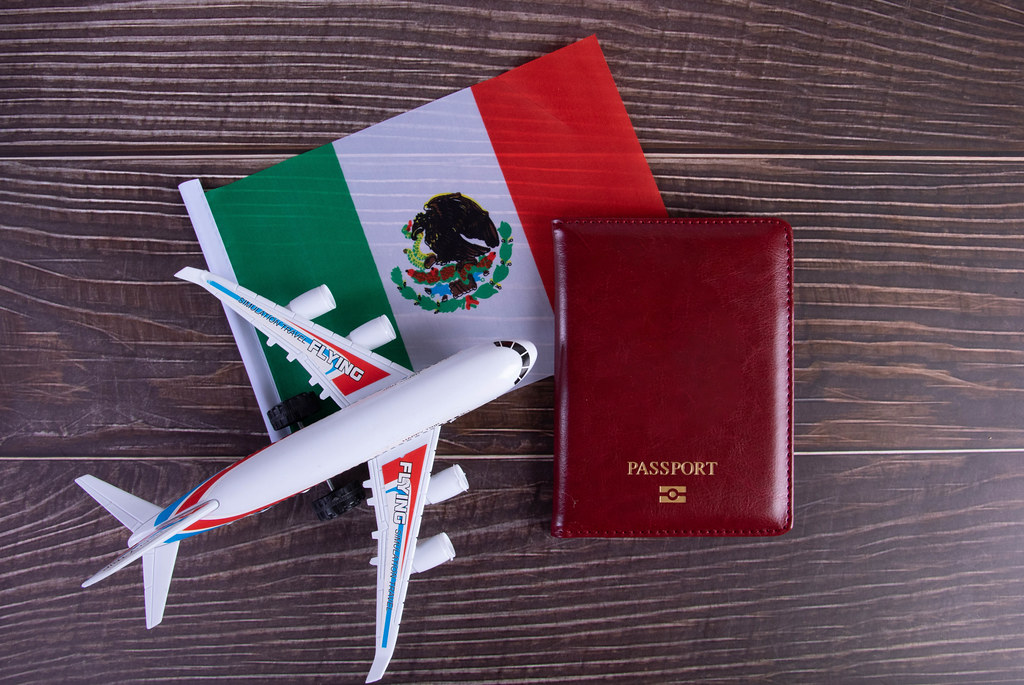 Passport, miniature airplane and flag of Mexico on wooden table