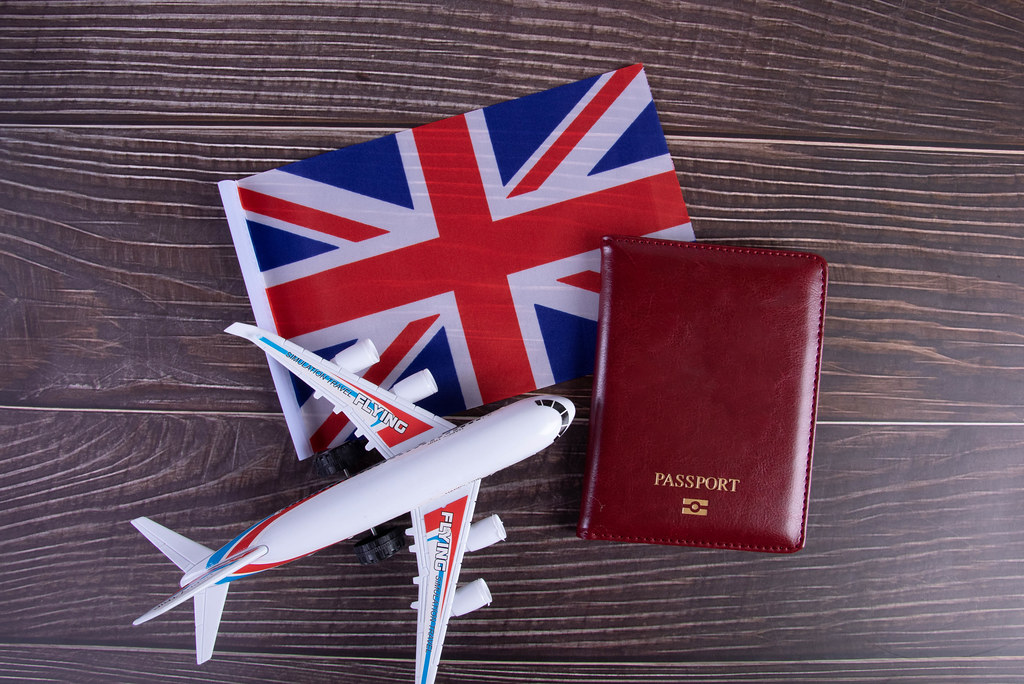 Passport, miniature airplane and flag of United Kingdom on wooden table