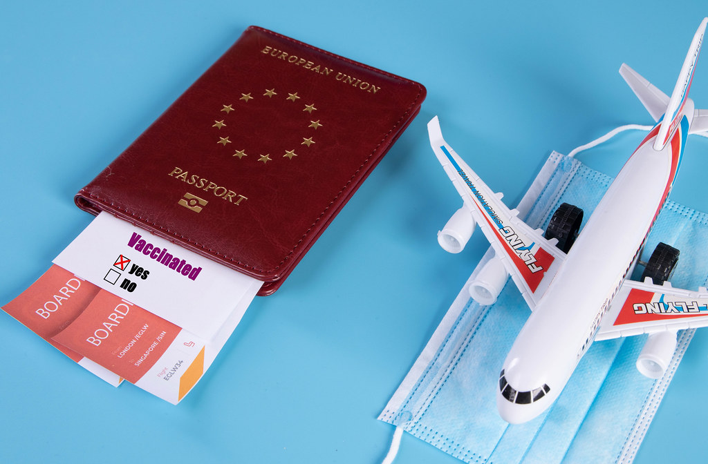 Passport with airline ticket, covid-19 vaccinated card with "Yes" mark and plane on blue background. Medicine and healthcare concept
