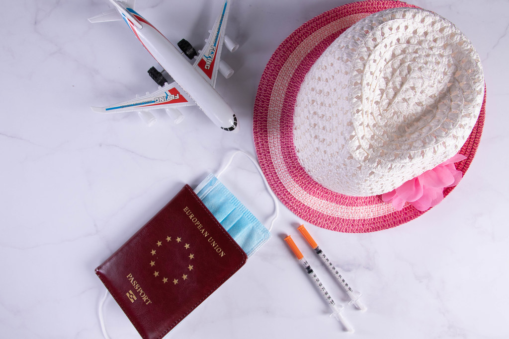 Passport with beach hat, small airplane and syringes