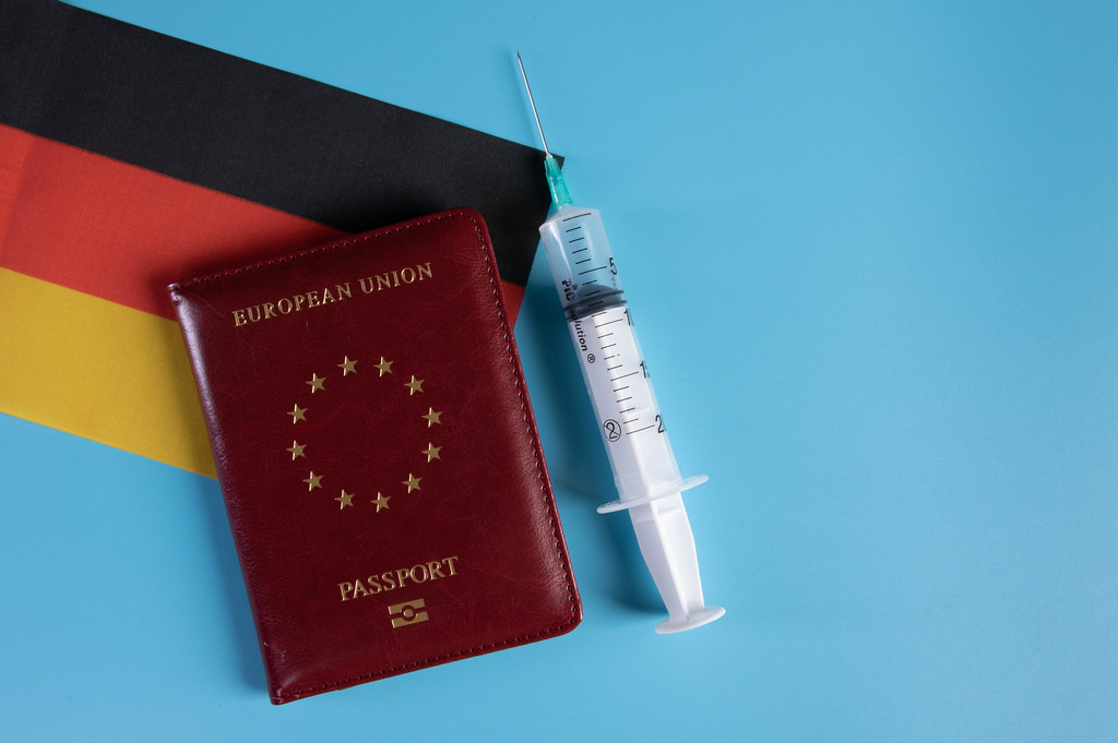 Passport with flag of Germnay and syringe on blue background