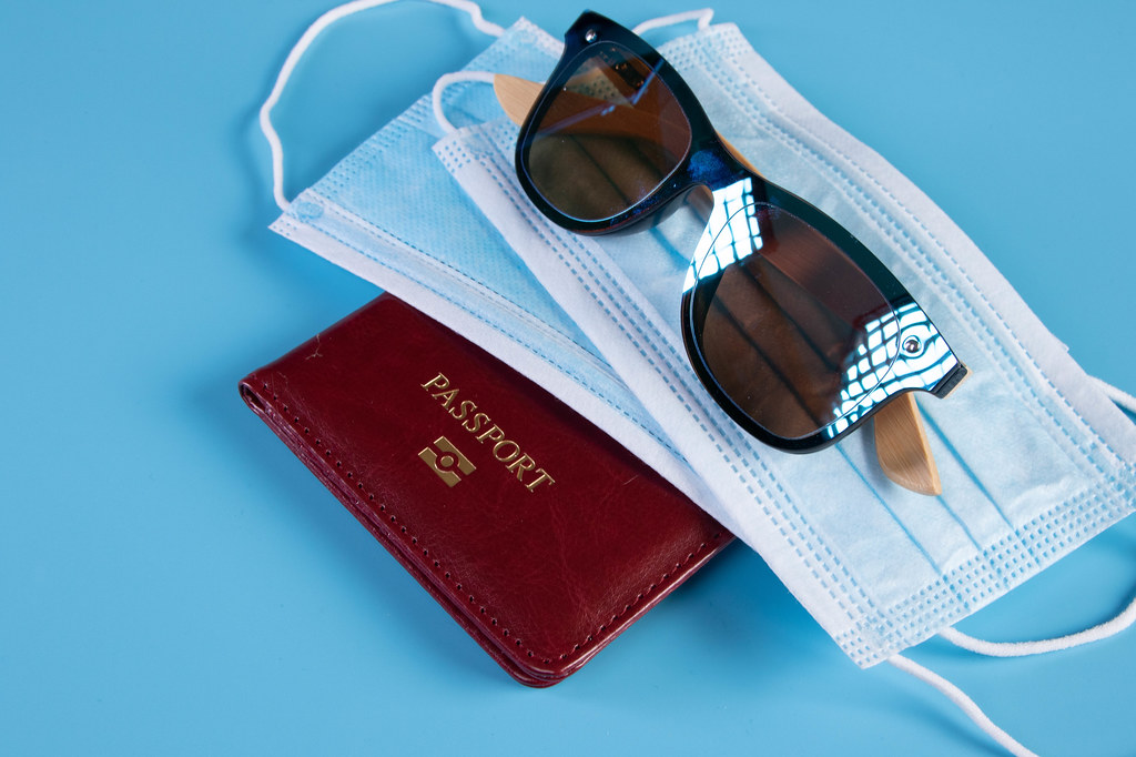 Passport with medical face mask and sunglasses on blue background