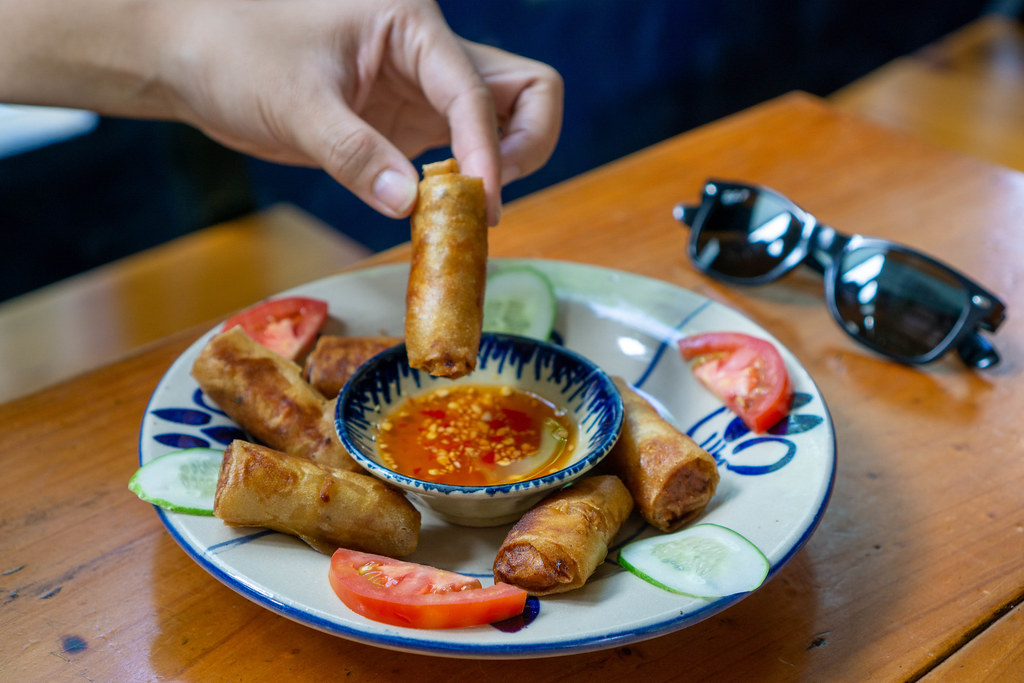 Person isst Vietnamesische fritierte Frühlingsrollen mit einem Dip aus Fischsauce und Chili mit der Hand in einem Restaurant