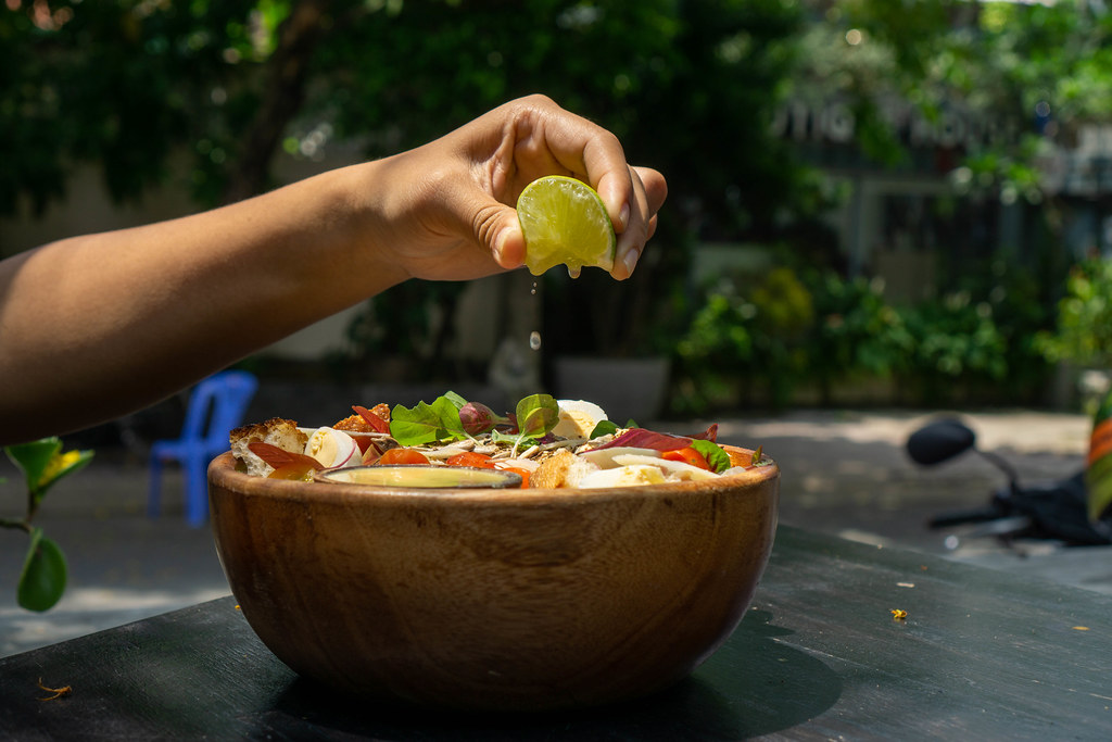 Person squeezes a Lime over a Healthy Salad Bowl with Basil, Boiled Quail Eggs, Honey Mustard Sauce and Chicken in a Garden of a Restaurant