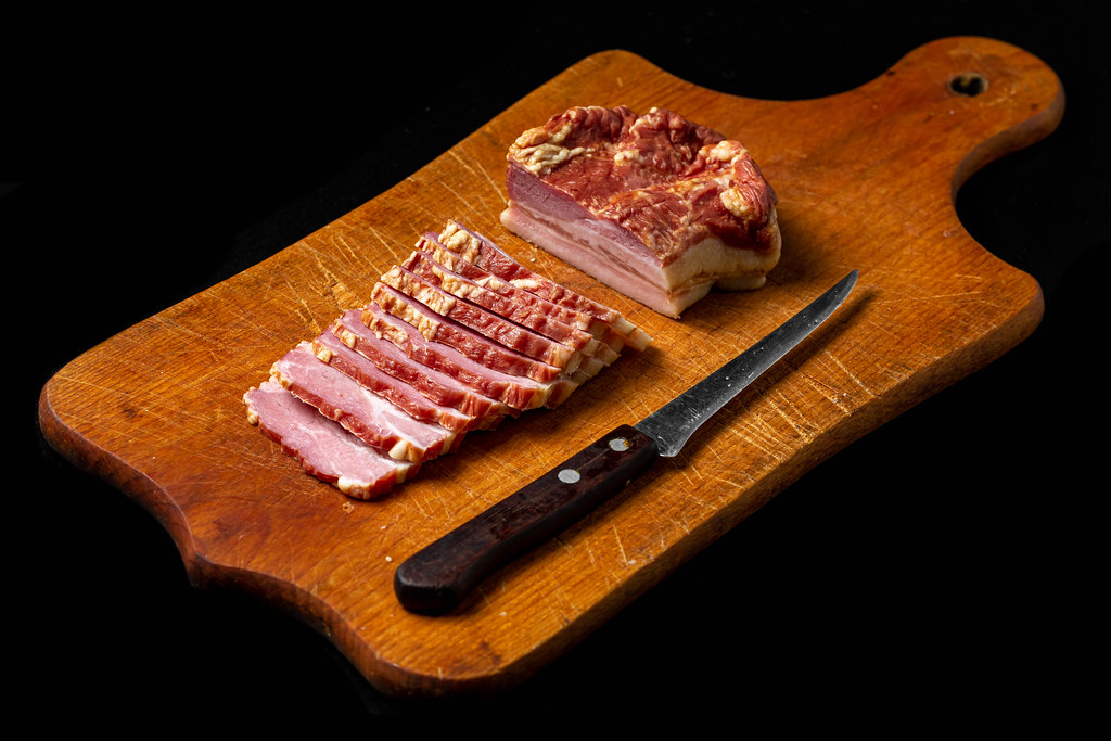 Pieces of smoked bacon on a cutting board with a knife