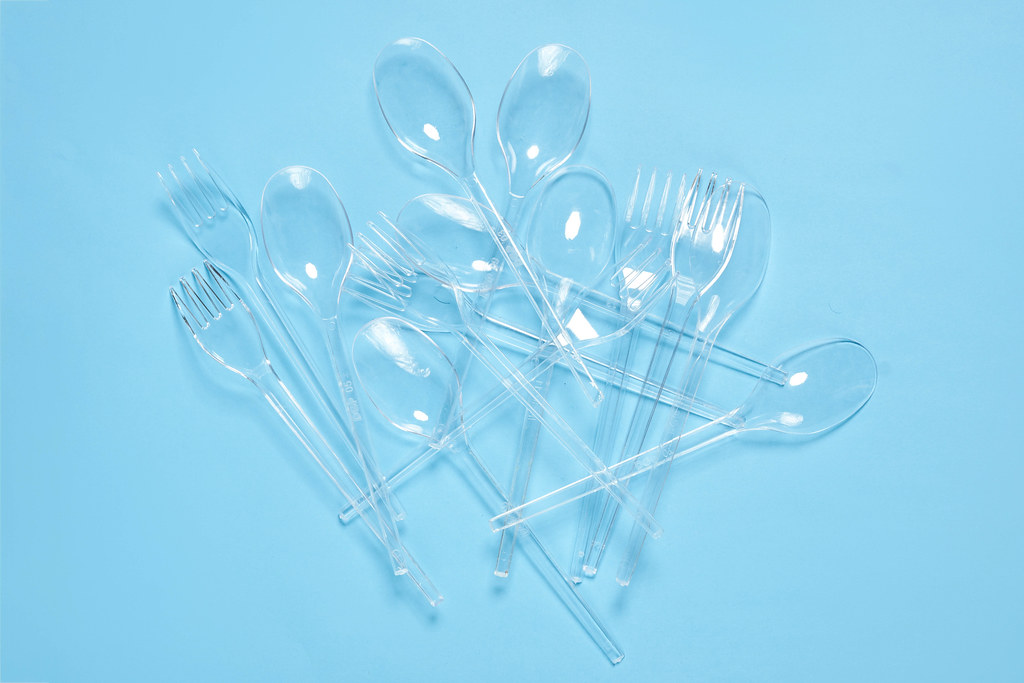 Pile of plastic spoons and forks on blue background