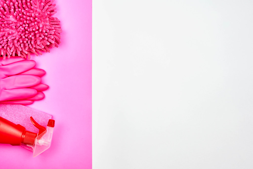 Pink-white background with cleaning products (mop, sponge, spray bottle, gloves) and copy space