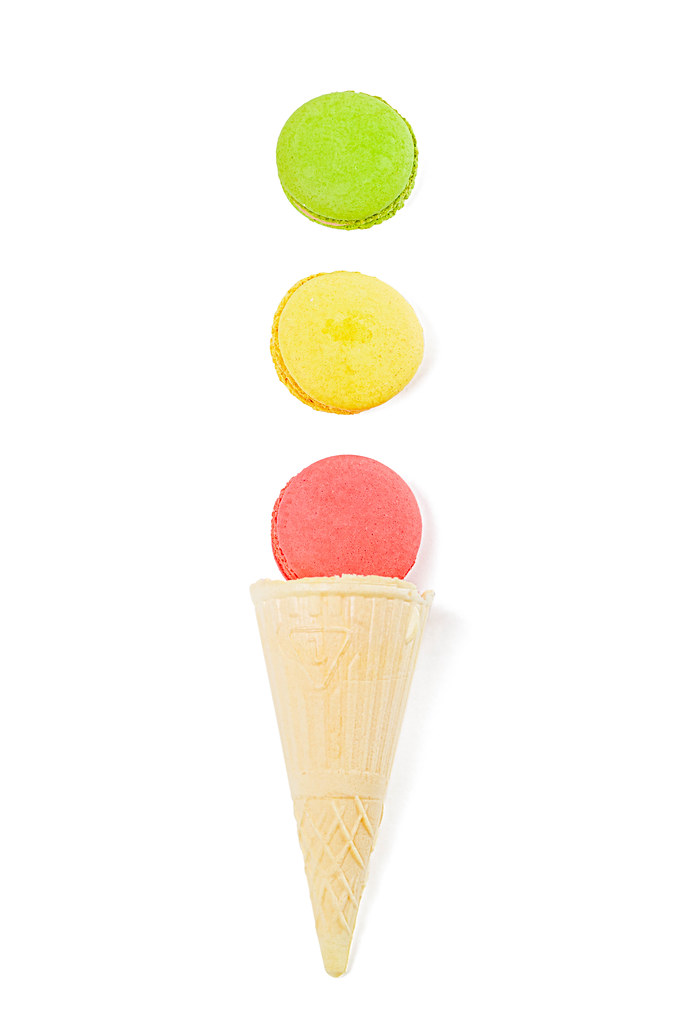 Pink, yellow and green macaroons on white background with waffle cone