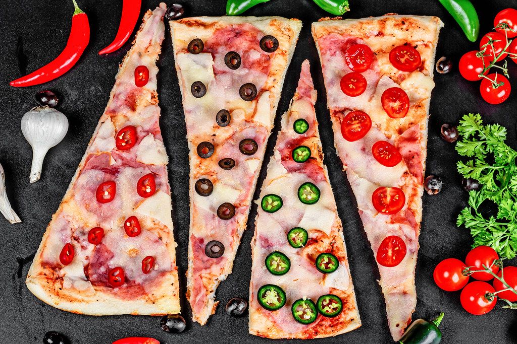 Pizza with ham, mozzarella, tomatoes, olives and hot pepper on a black background, top view