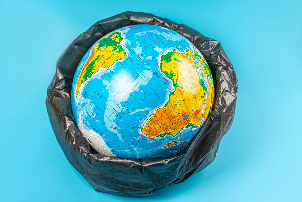 Planet earth in plastic bag on blue background. Concept - ecology, planet pollution with plastic cellophane polyethylene earth day, world environment day