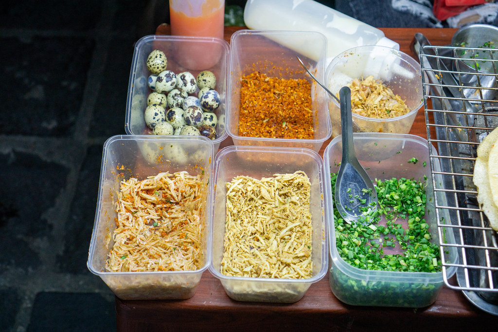 Plastikschalen mit Zutaten wie Wachteileier, Chili, Frühlingszwiebeln und Shrimps für Vietnamesische Pizza Banh Trang Nuong bei einer Straßenküche in Hoi An, Vietnam
