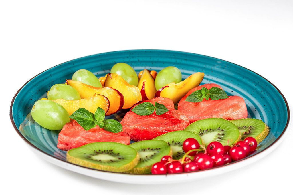 Plate with sliced ripe fresh fruit and berries