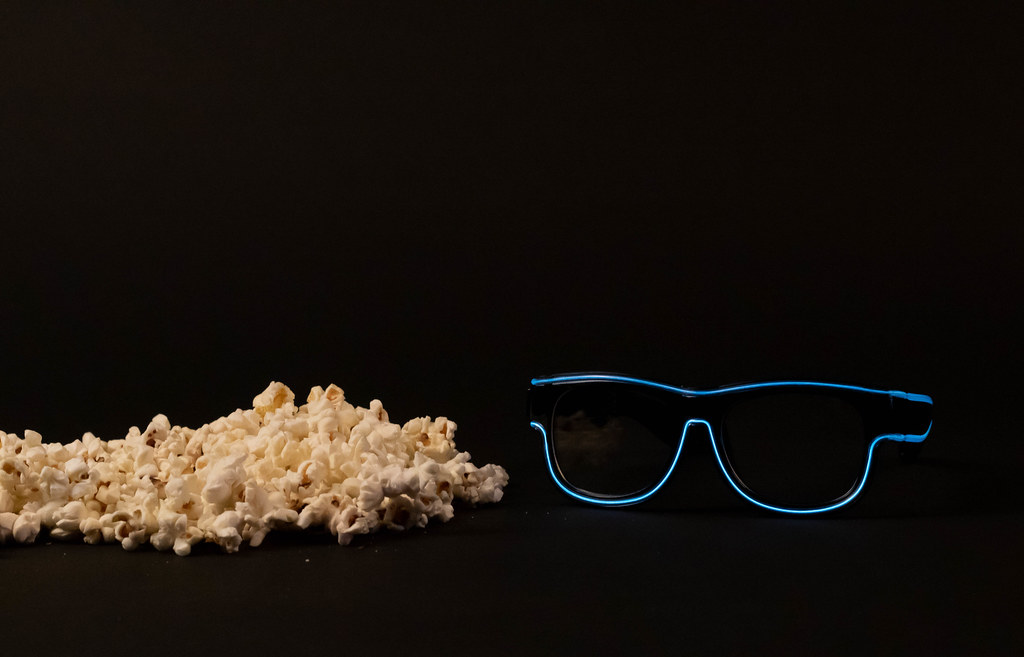 Popcorn and neon glasses on black background