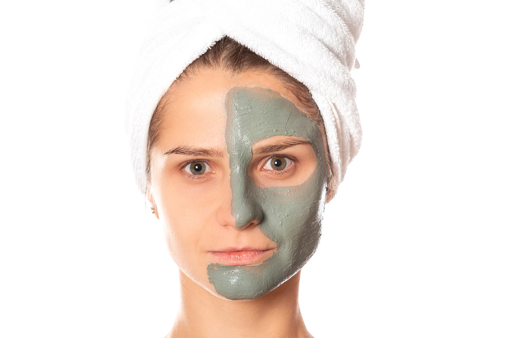 Portrait of a woman with a clay mask applied to half of her face
