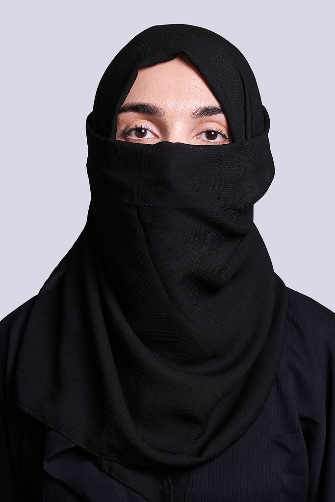 Portrait of muslim woman in traditional Islamic cloth niqab against on gray background