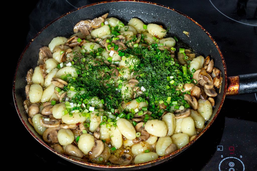 Potato gnocchi with mushrooms, onions and herbs in a frying pan on the hob