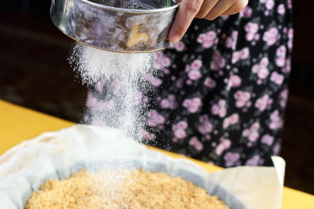 Powdered sugar is poured out of a sieve on a cheesecake