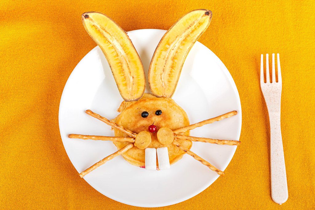 Rabbit face with pancake, berries and banana on yellow background, top view