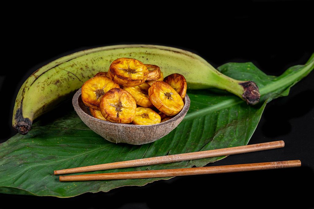 Raw and fried plantain on dark background with green leaf