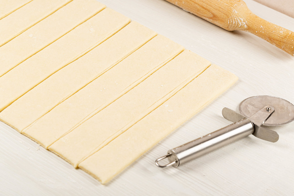 Raw dough cut into strips on a table with a knife and rolling pin
