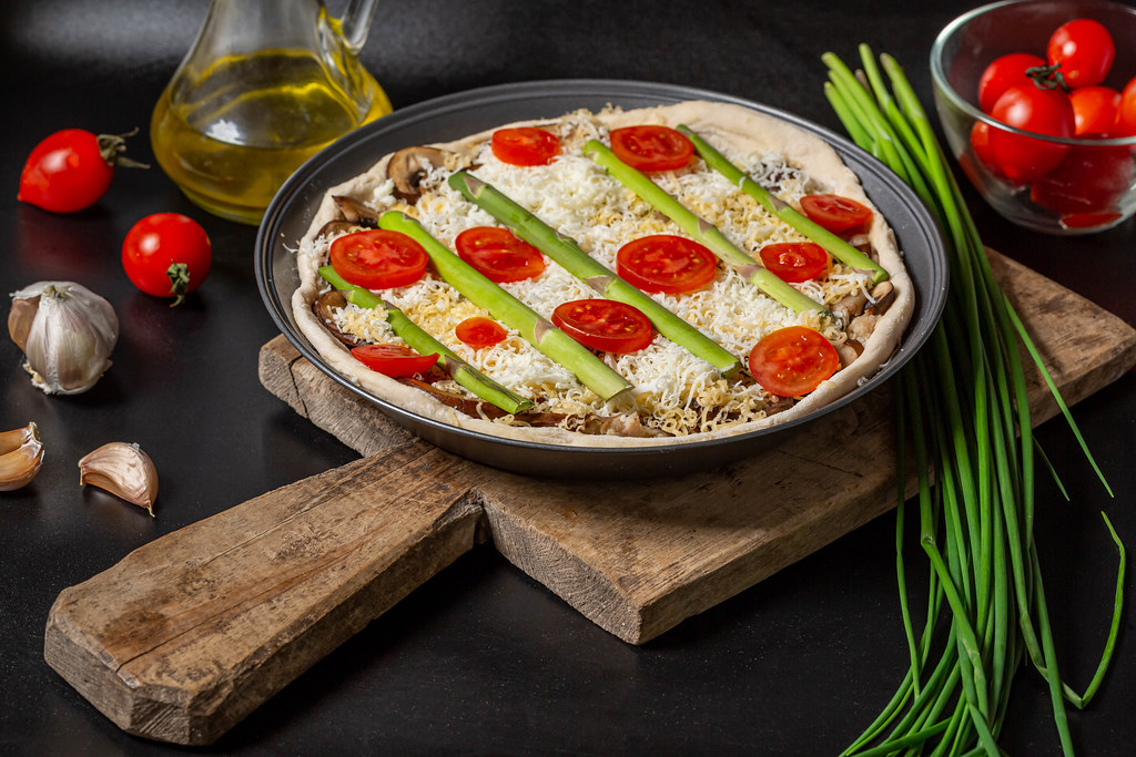 Raw pie with minced meat, mushrooms, cheeses and vegetables on a dark background